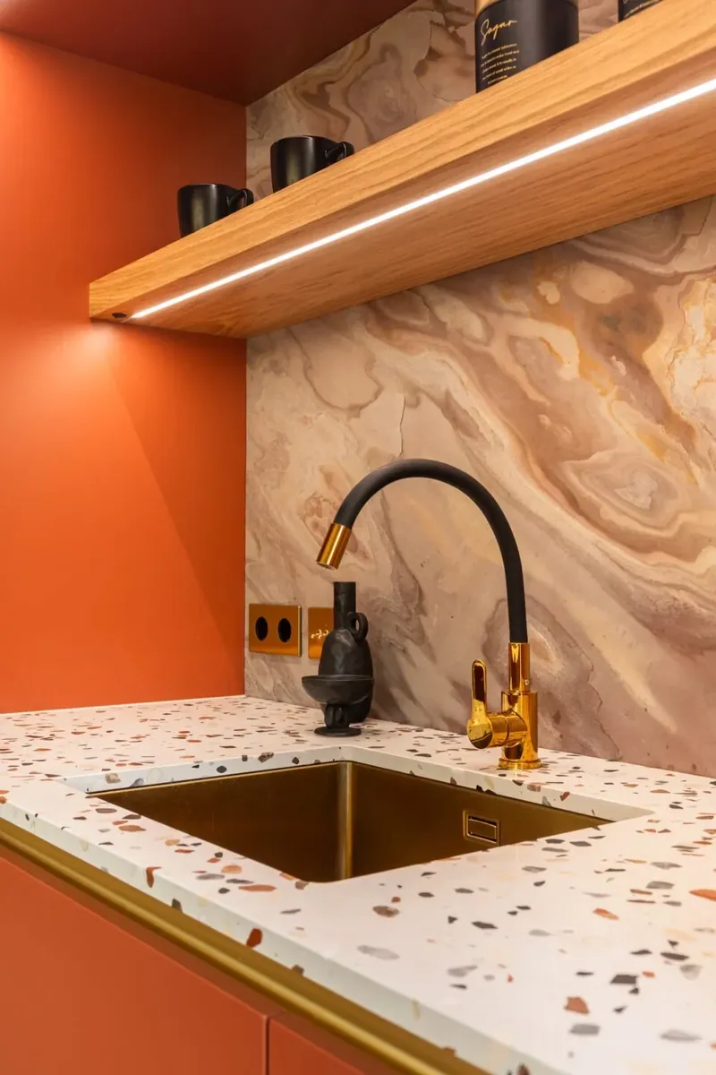 Szczedrzyk house: brass sink and black tap under a lit oak shelf and marble splashback