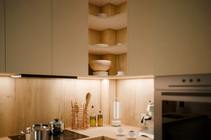 Render of a cream kitchen corner with oak shelves and warm under-cabinet light